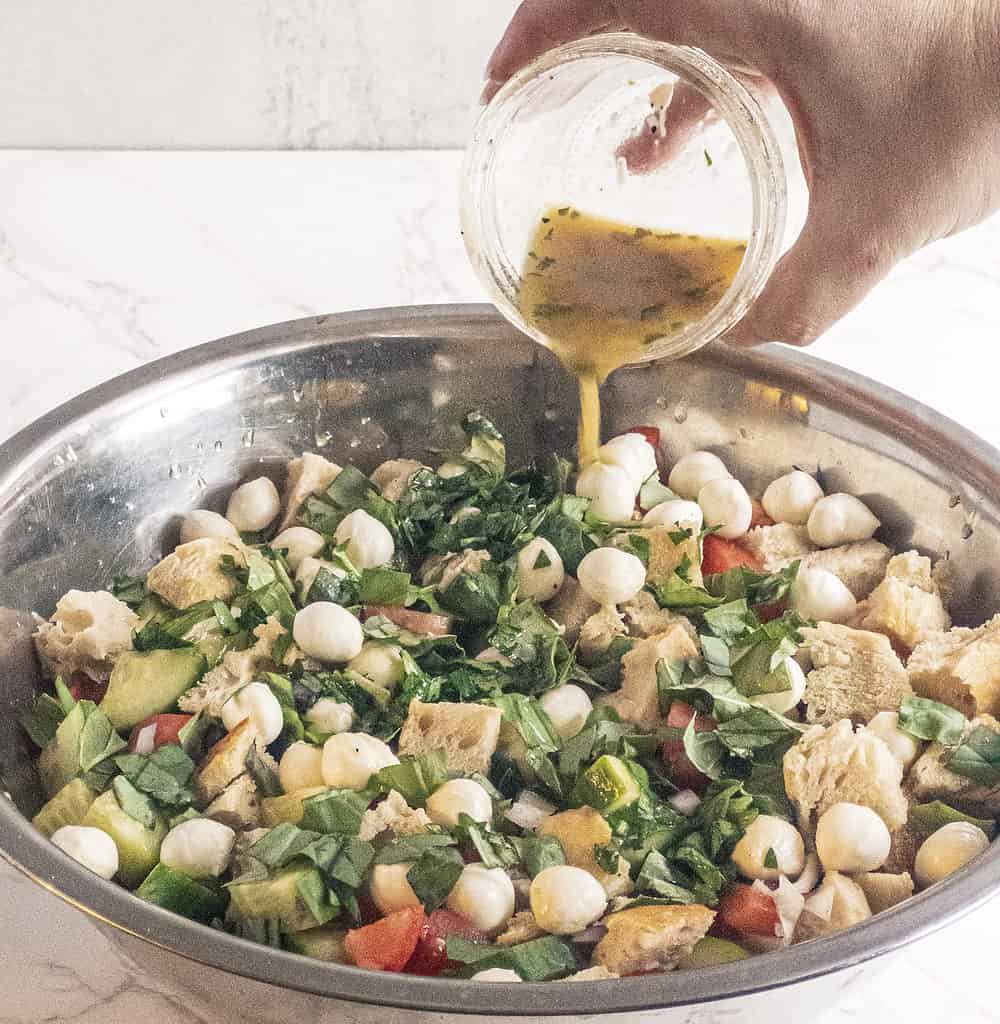 Panzanella salad in bowl with dressing pouring over