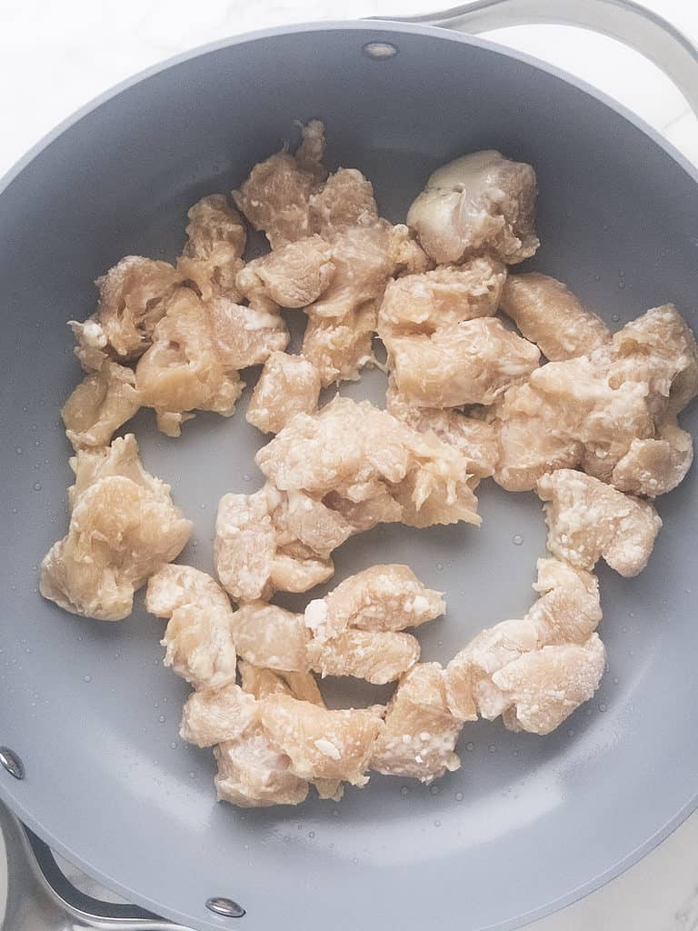 process shot of cornstarch coated uncooked chicken in a skillet