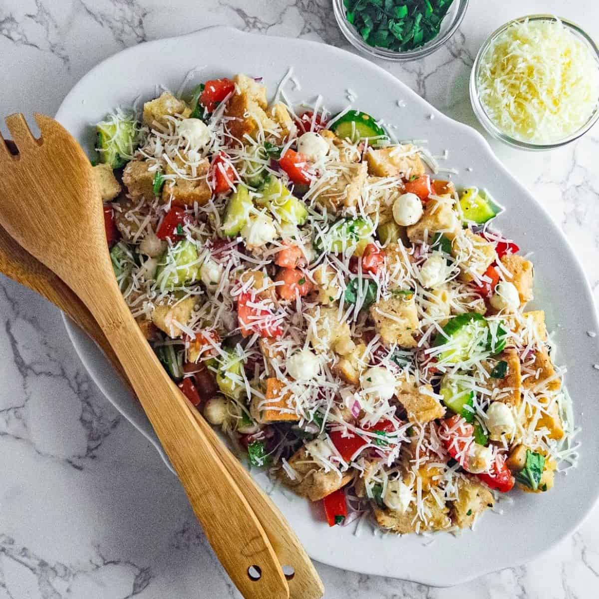 panzanella salad on a platter with wooden serving spoons