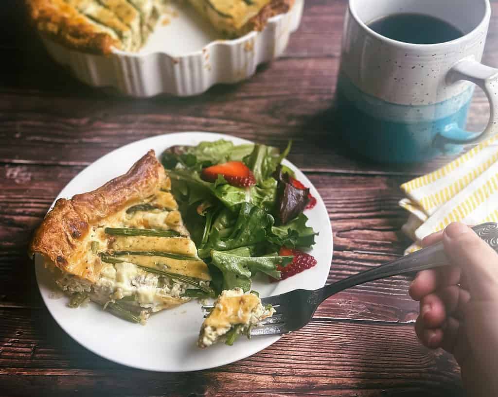 asparagus and ricotta tart on a plate with mixed green strawberry salad and fork with a bite of tart