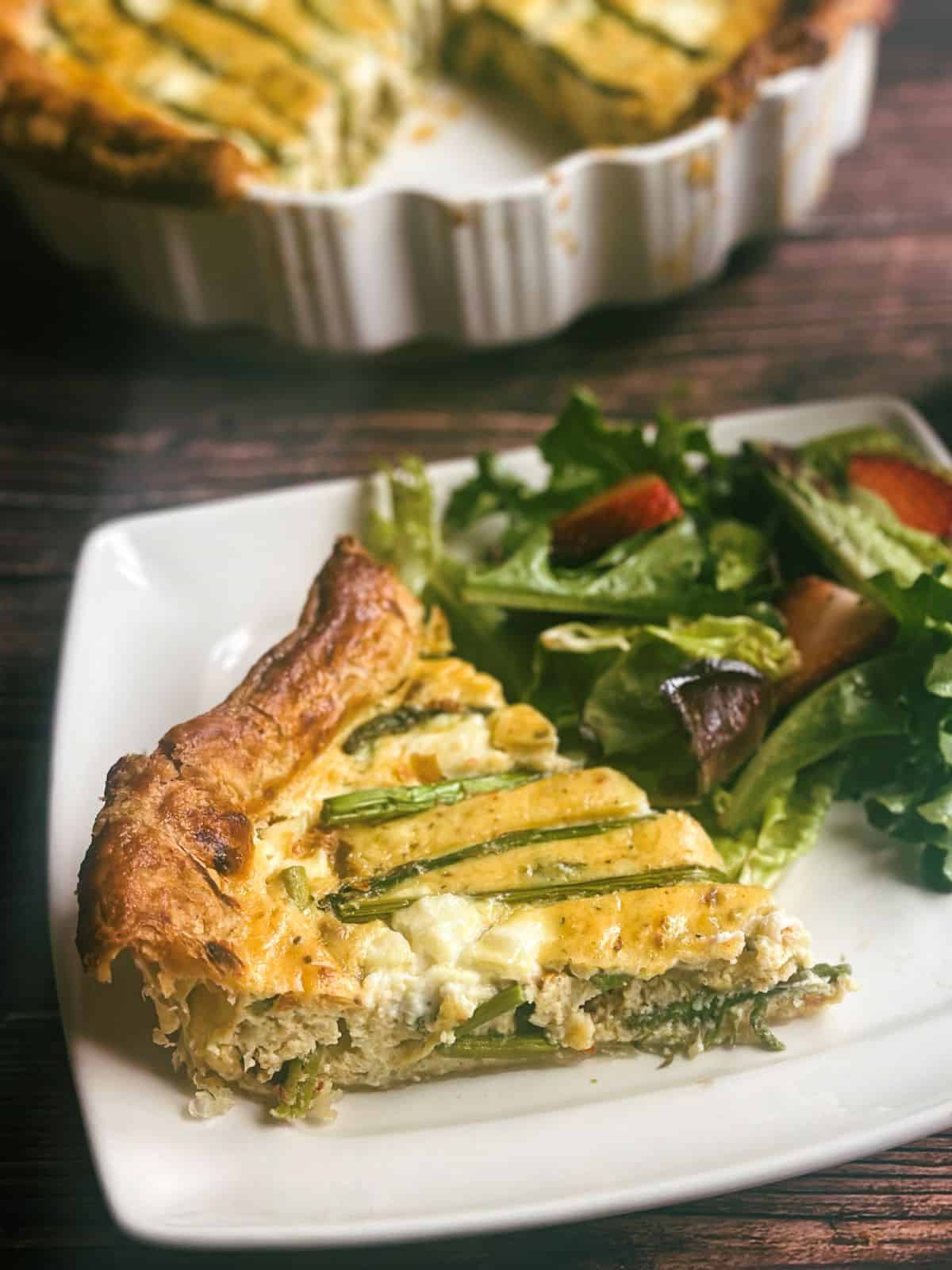 slice of asparagus ricotta tart on white plate with strawberry spring mix salad