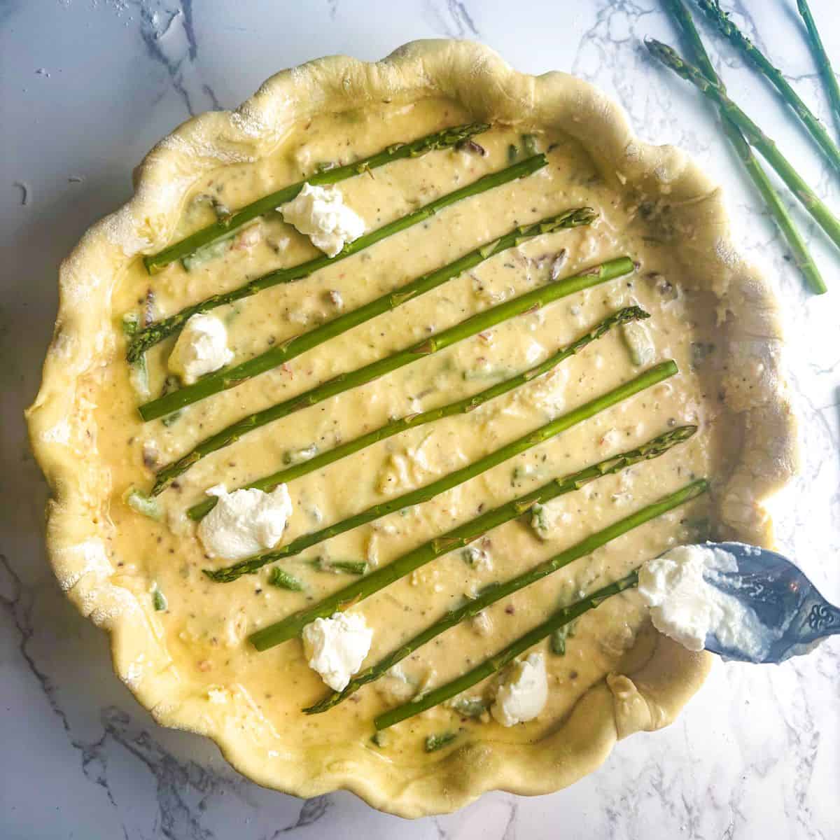 asparagus ricotta tart with spoon adding dollops of ricotta cheese