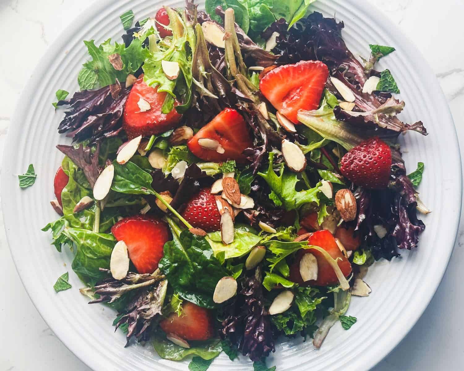 Strawberry spring mix salad with toasted almond slices in large white serving bowl.