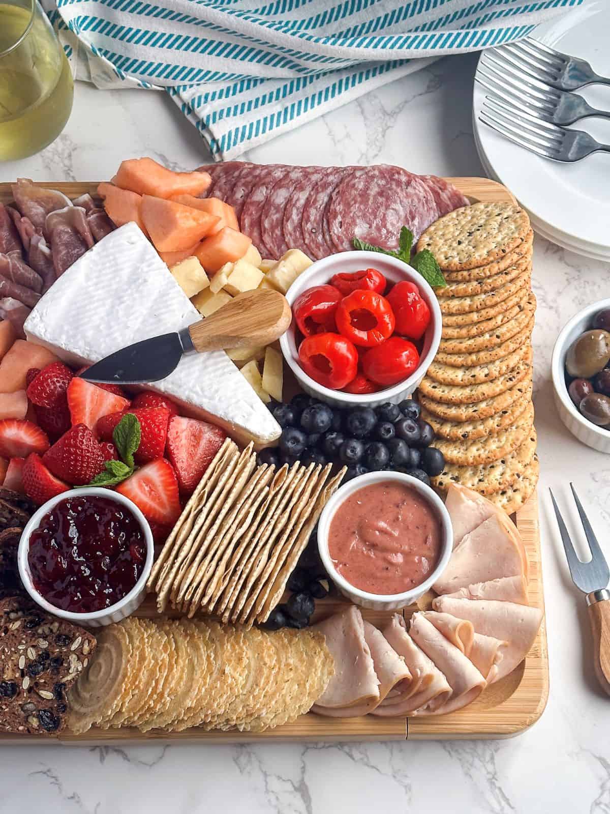 Square charcuterie board with crackers, fruit, and spreads.