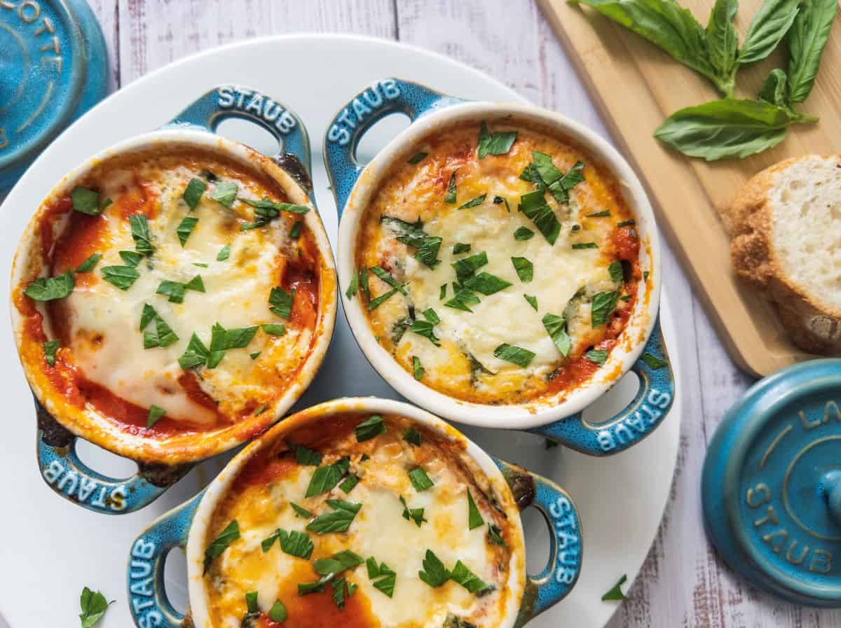 Baked eggs with cheese and tomato sauce in three small Staub cocotte dishes.