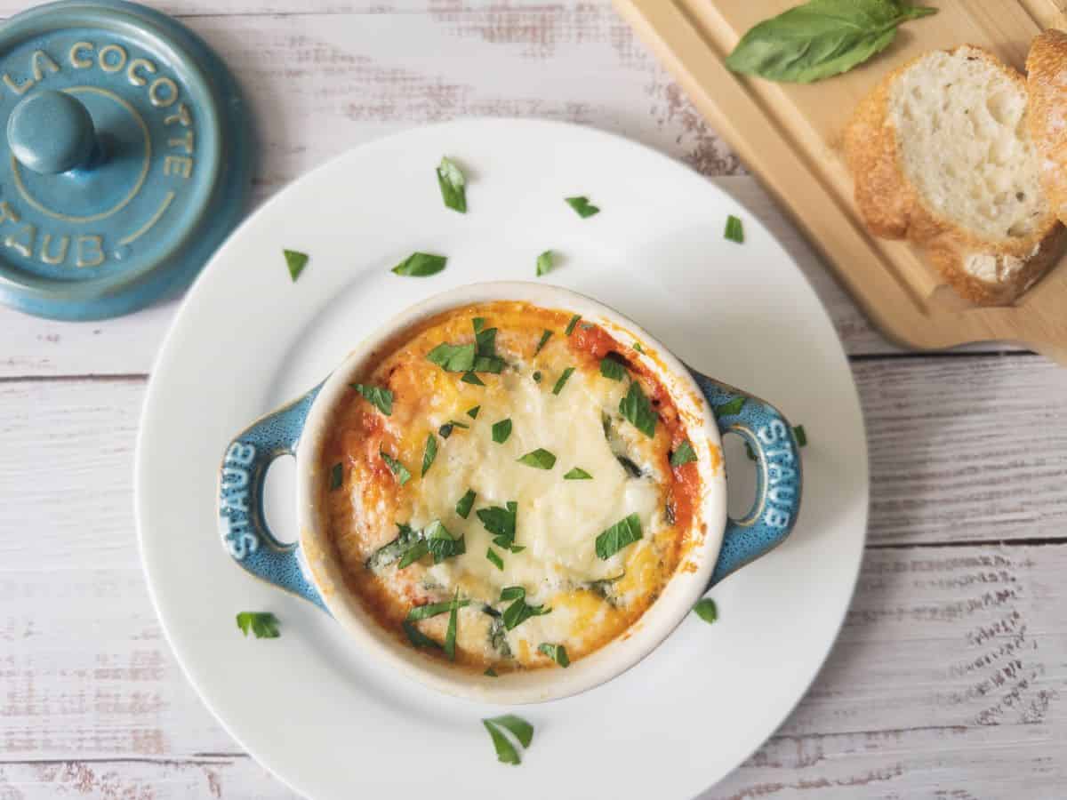 Italian baked eggs in a mini cocotte dish with fresh basil garnish.