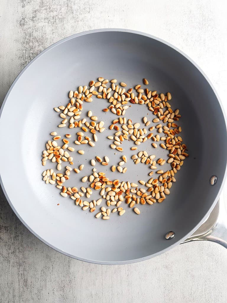 Toasted pine nuts in a skillet.