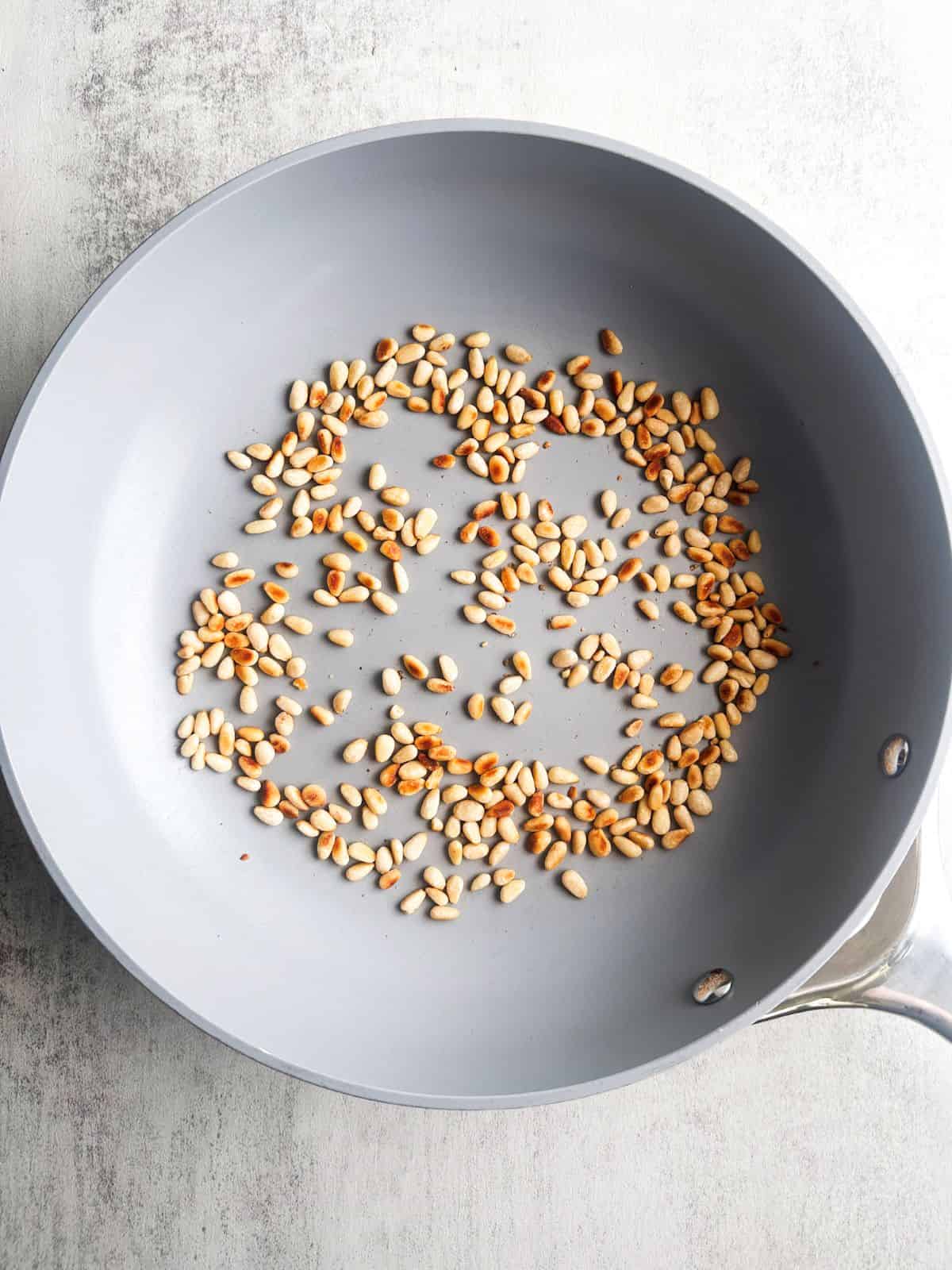 Toasted pine nuts in a skillet.