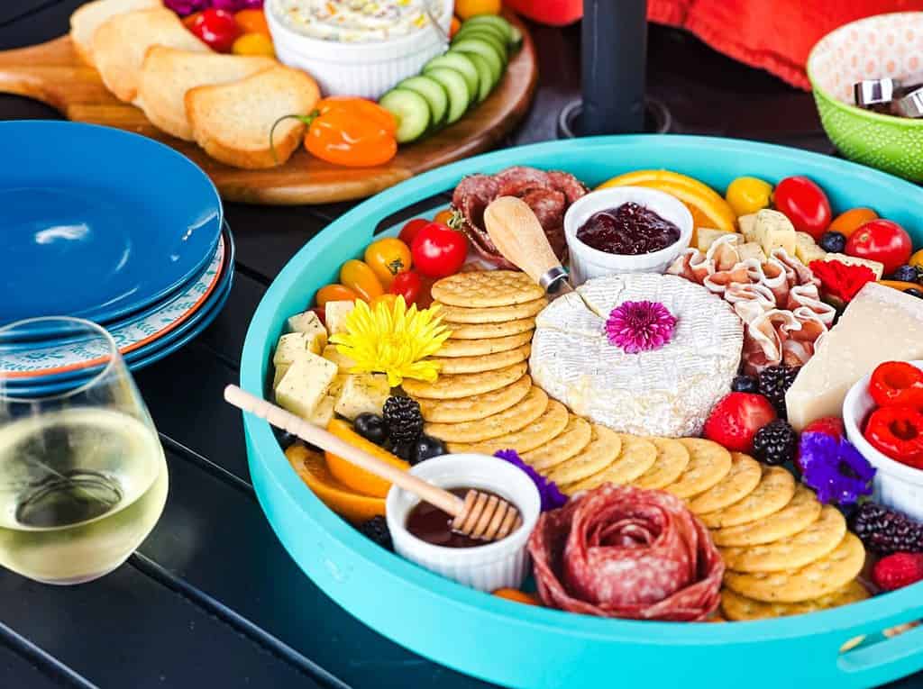 Charcuterie, crackers, fruits, and veggies on a table with wine and plates.