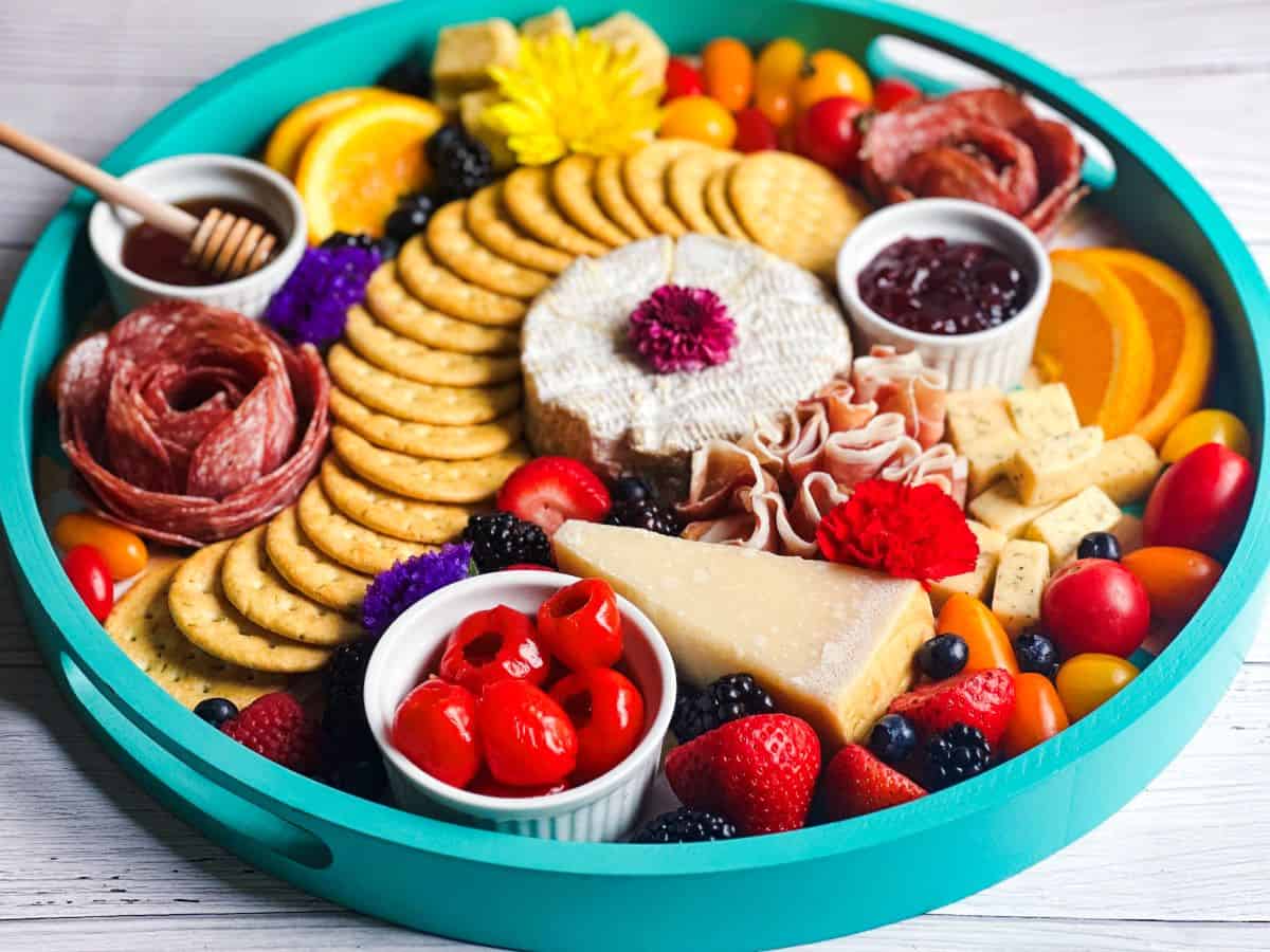 Blue charcuterie board with cheese, crackers, fruits, and flowers.