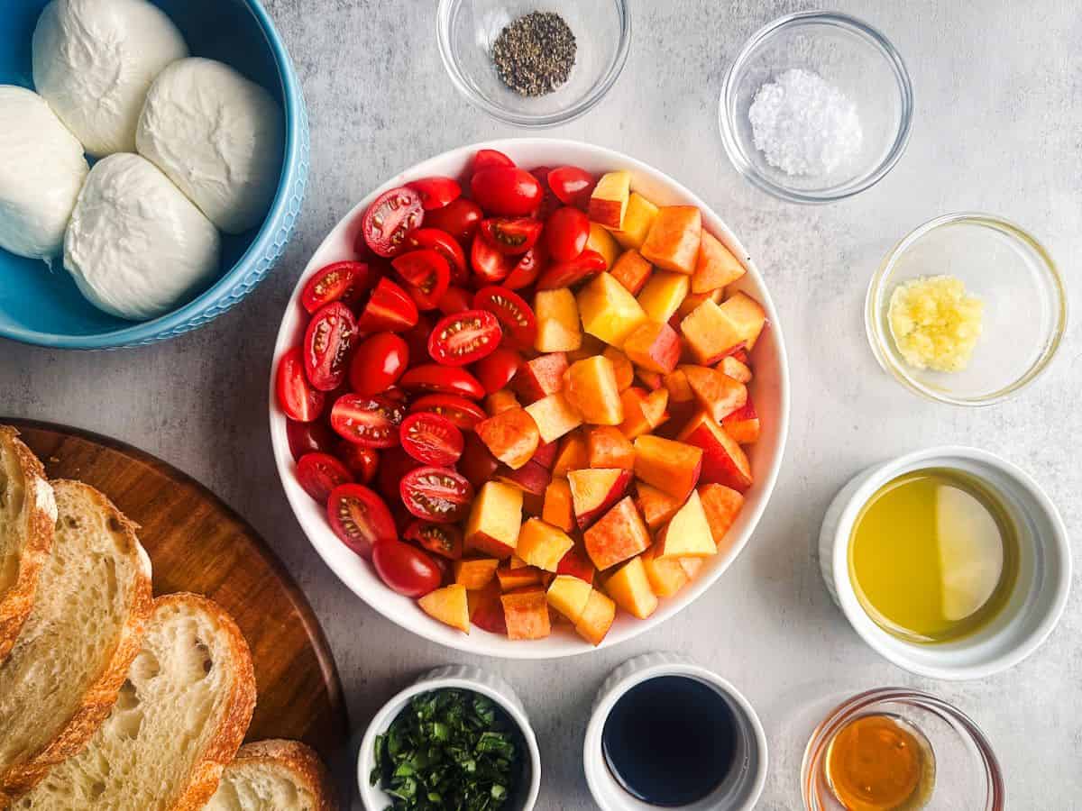 Chopped peaches and tomatoes, sliced bread, burrata cheese, and other ingredients in small ramekins for burrata bruschetta recipe.