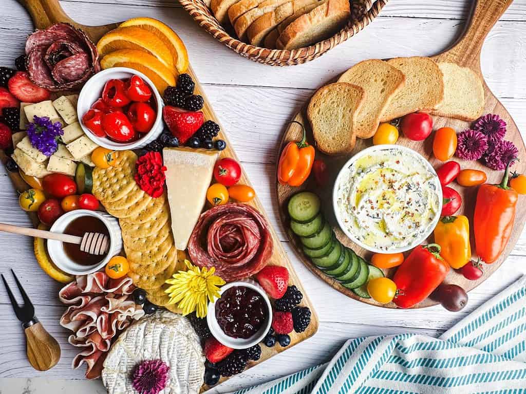 Two charcuterie boards with meats, cheeses, veggies, fruits, flowers and whipped ricotta dip.