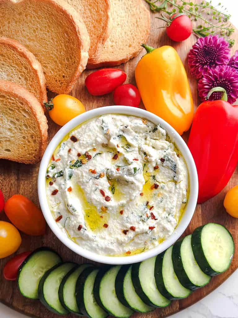 Whipped ricotta dip on a wooden charcuterie board with veggies and crostini.