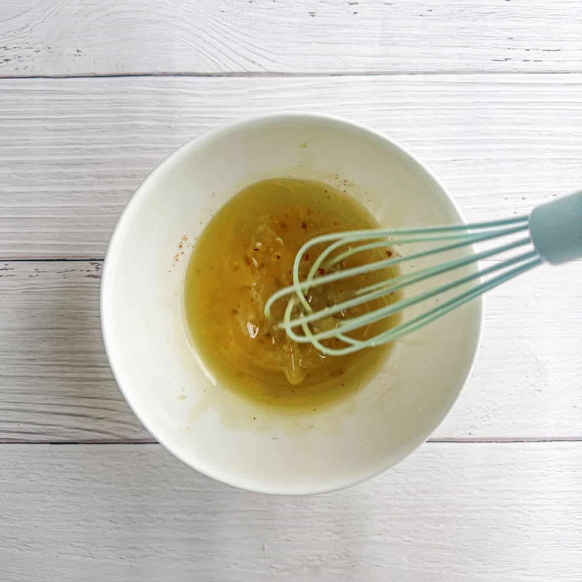 Dressing being mixed with a whisk in a white bowl.