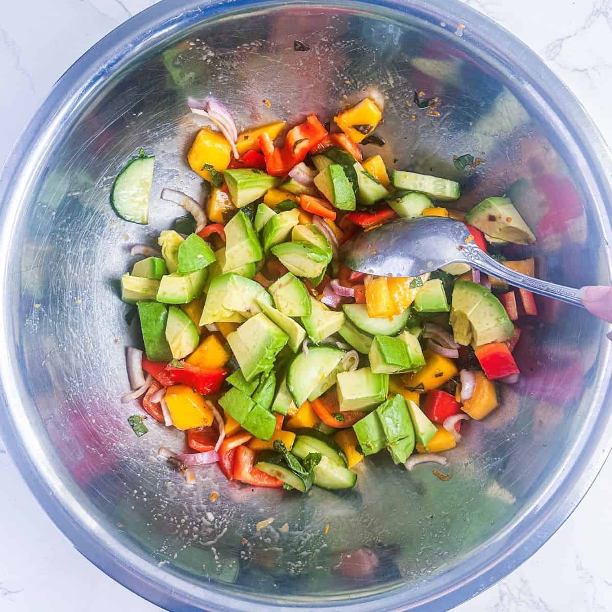 Avocado, cucumber, mango, shallots, bell pepper, and mint in a silver mixing bowl.