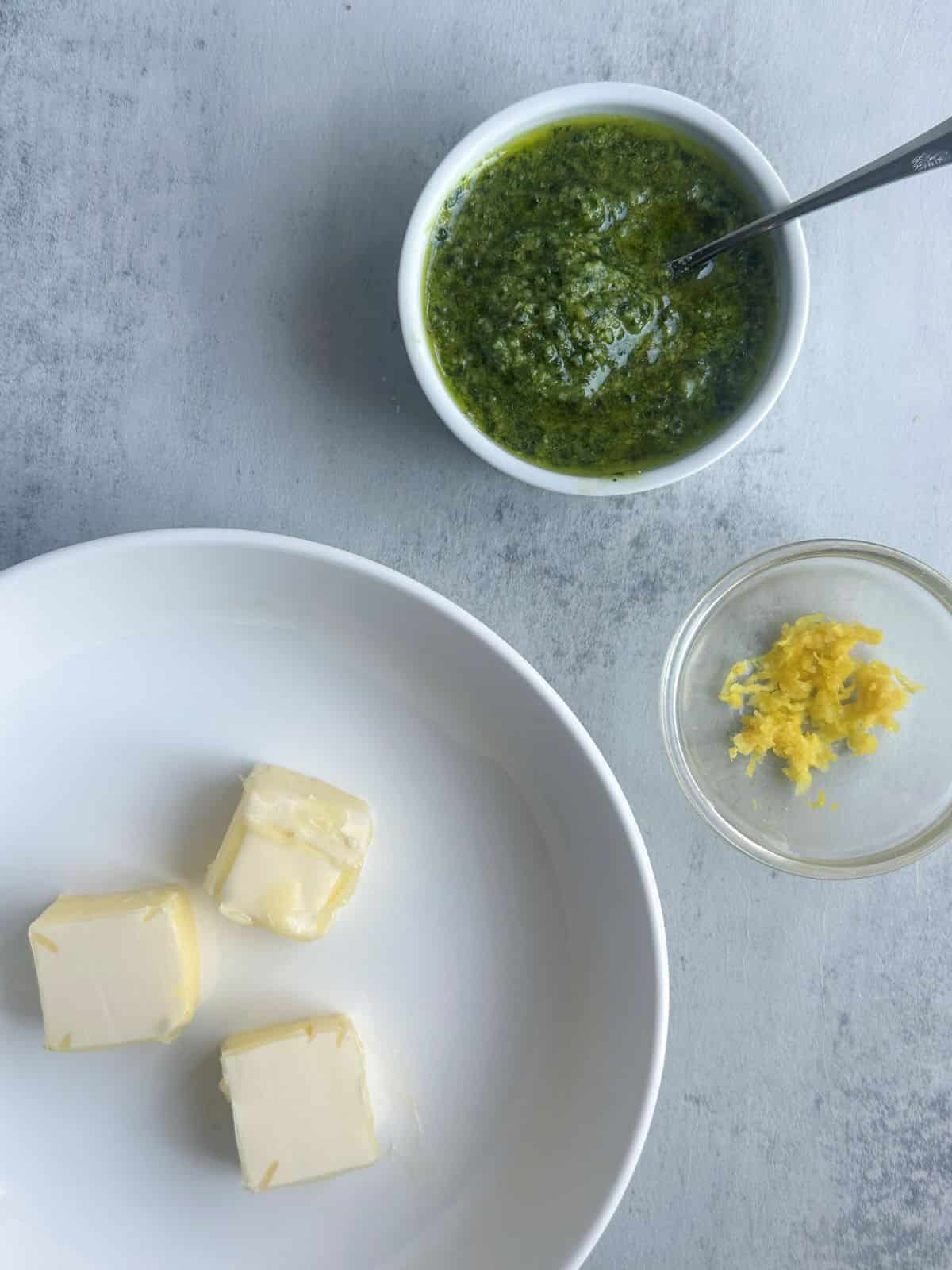 Slices of butter, pesto, and lemon zest in small bowls.