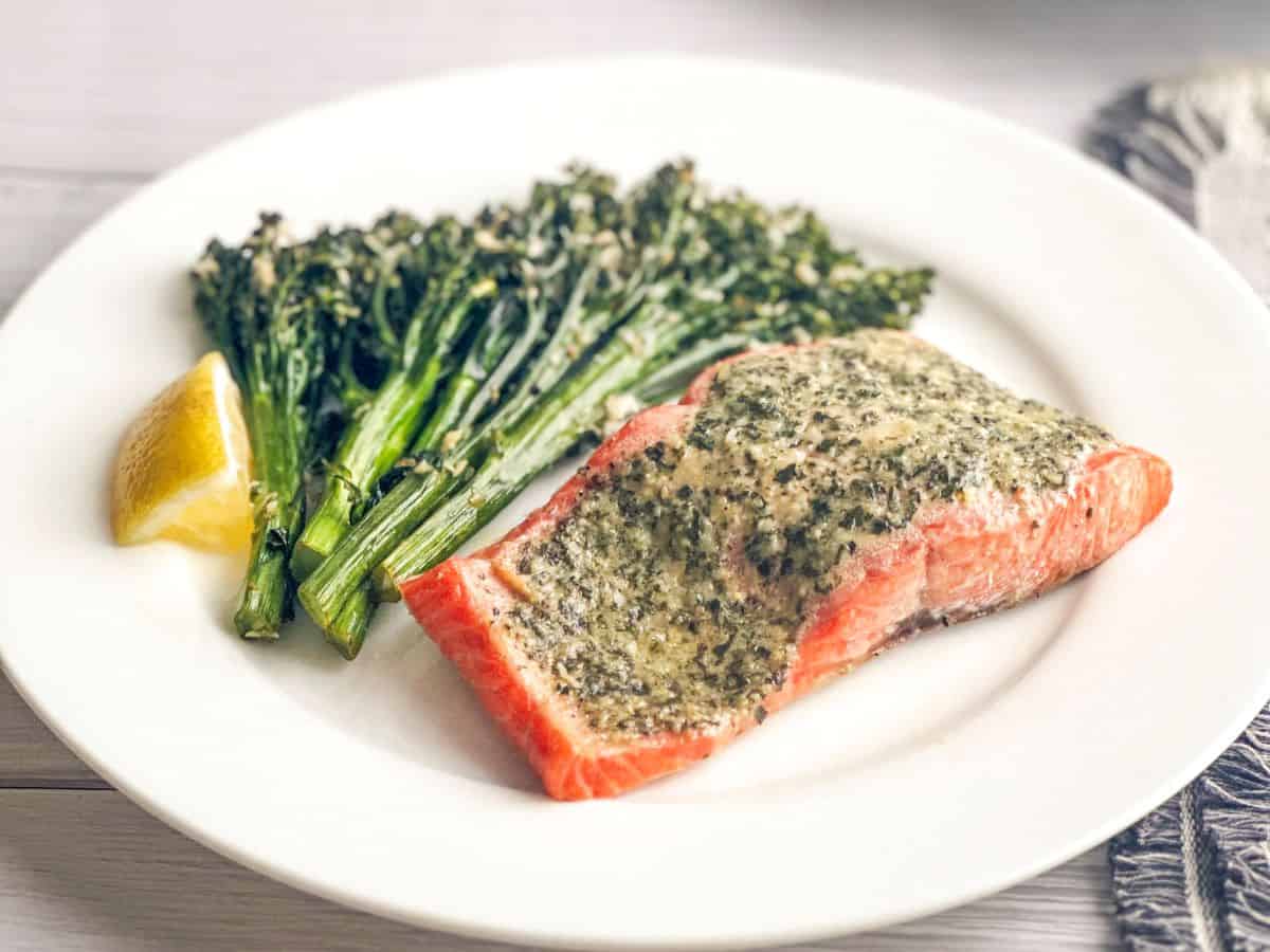 Pesto butter salmon milano and broccolini on white dinner plate.