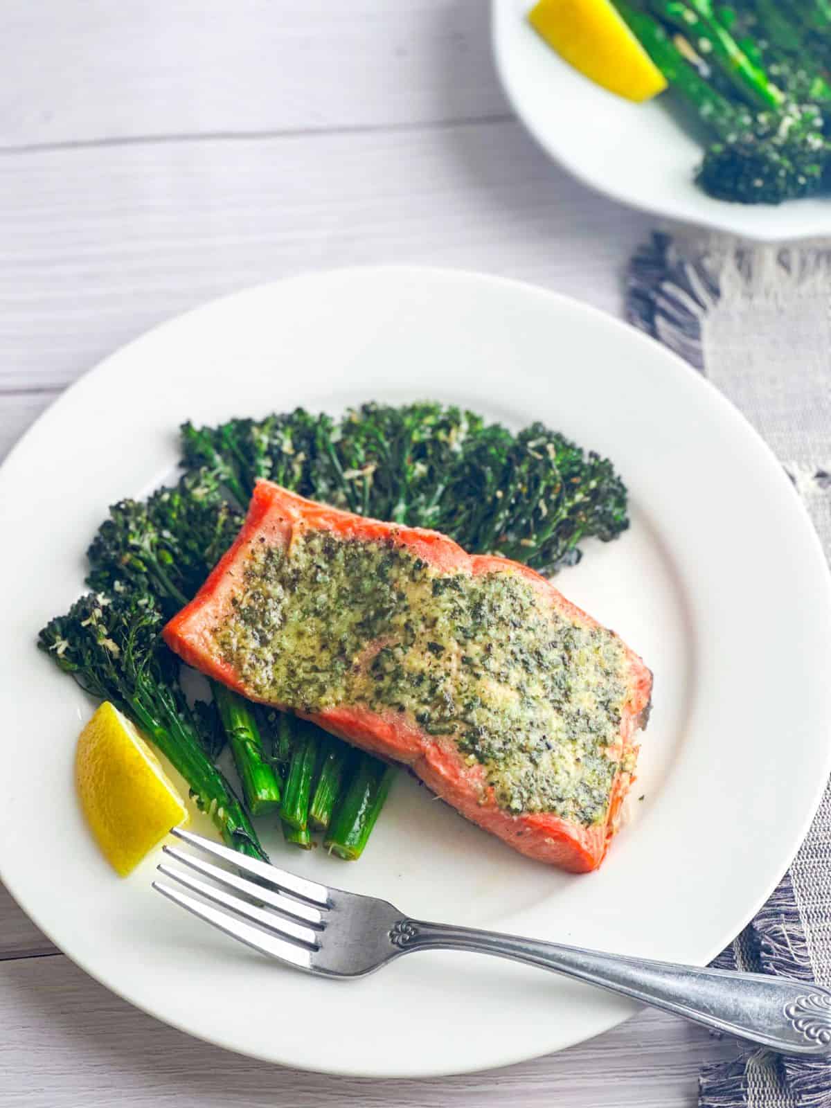 Pesto butter topped salmon with broccolini and a fork on a white plate.