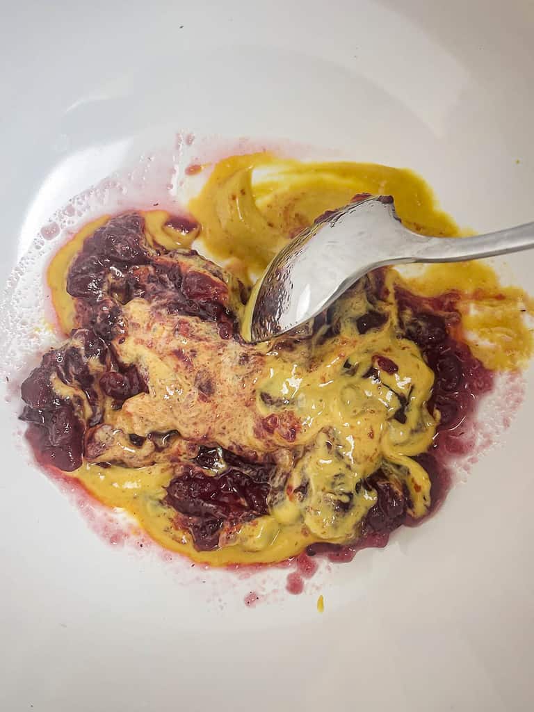 Cranberry sauce and honey mustard being mixed together in a bowl with a spoon.