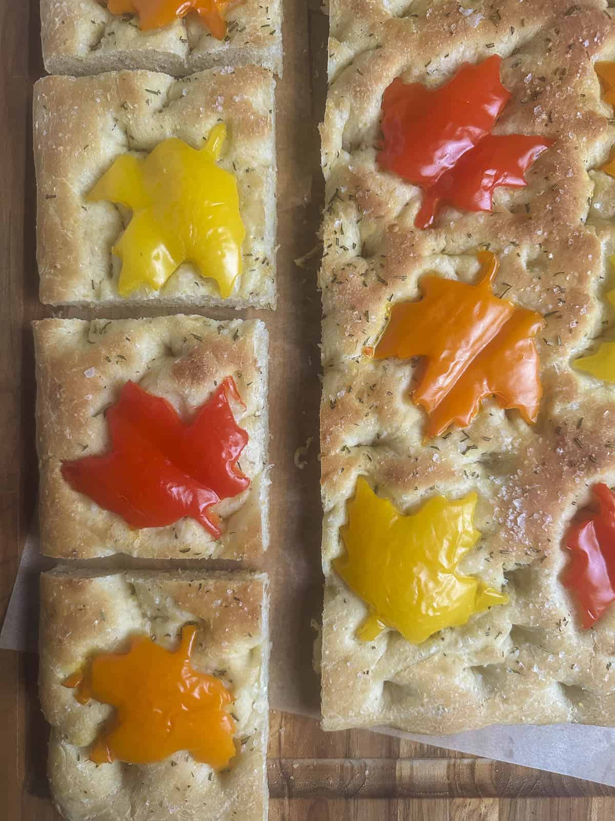 Fall focaccia bread squares with maple leaf shaped red, orange, and yellow bell peppers.