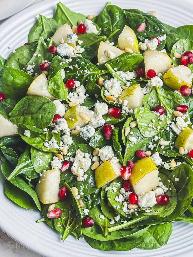 Spinach and Gorgonzola salad with pear and pomegranate in a white serving bowl.