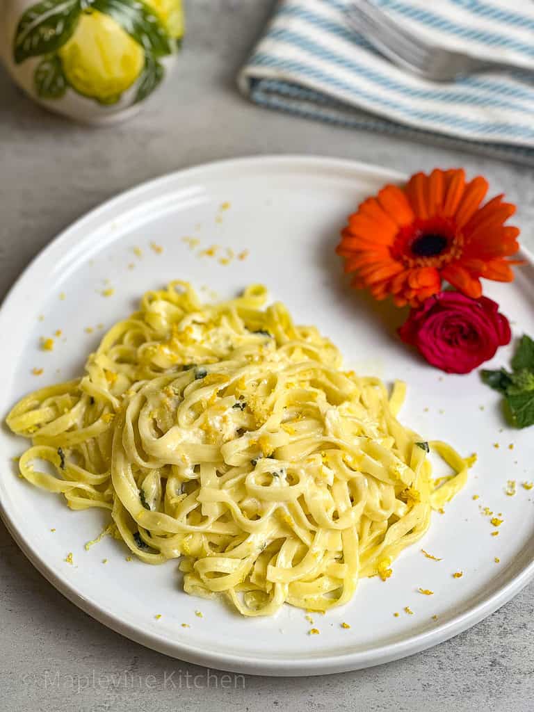 Linguine noodles in a creamy citrus sauce on a white plate with fresh orange and red flowers as a presentation garnish.