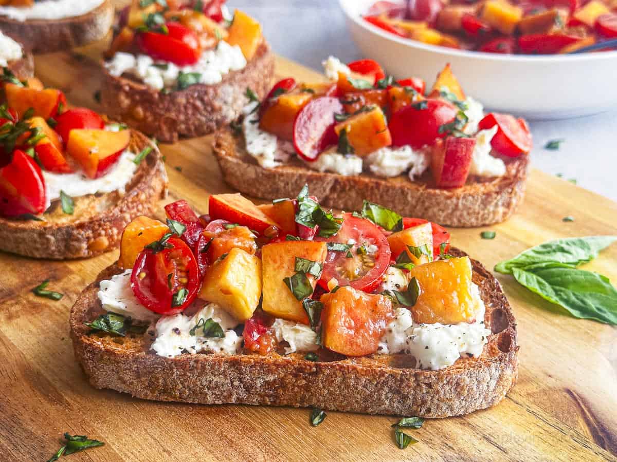Peach and tomato burrata bruschetta on toasted bread with fresh basil leaves.