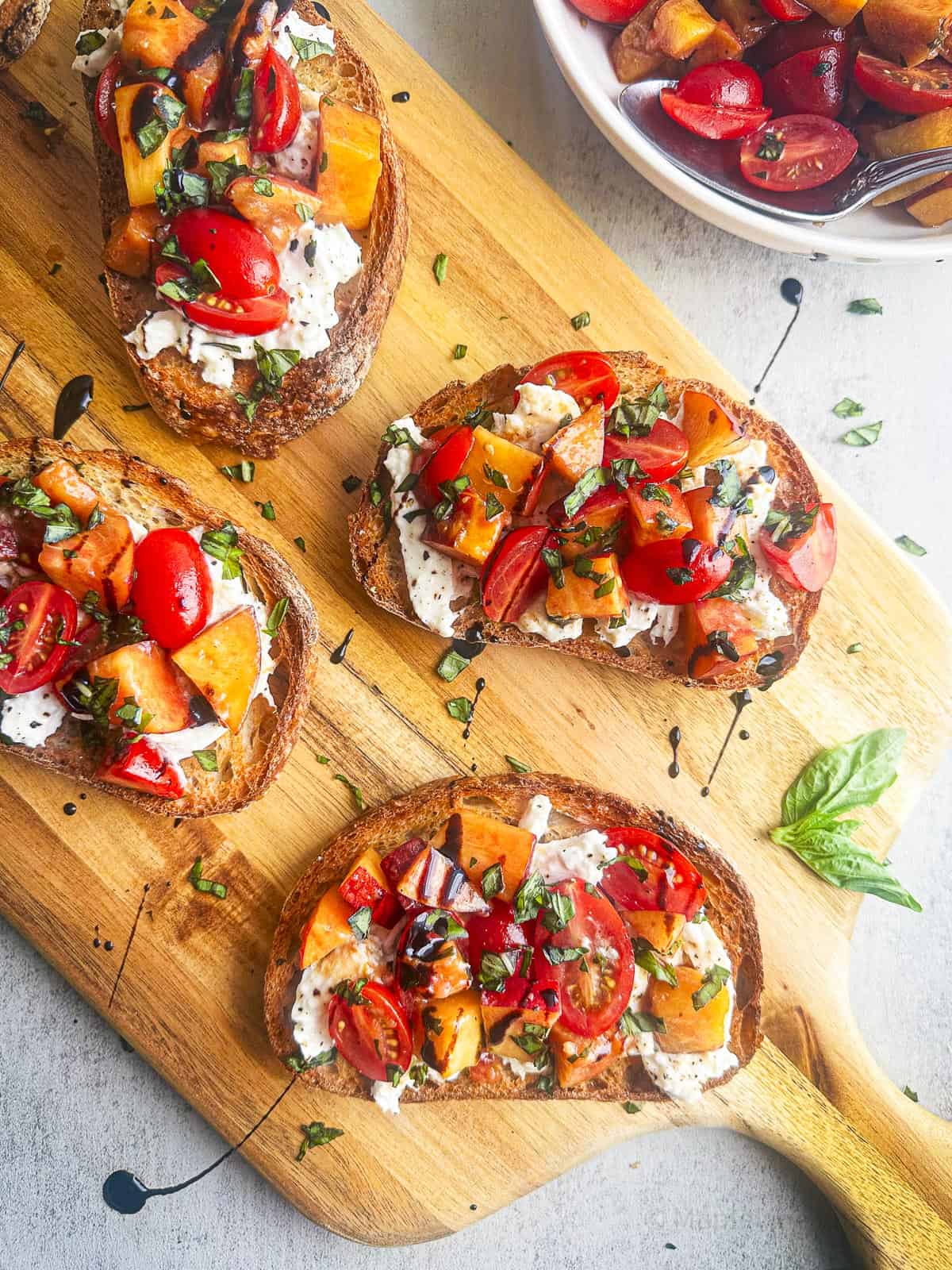 Burrata bruschetta on toasted bread with peaches, tomatoes, and fresh basil leaves.