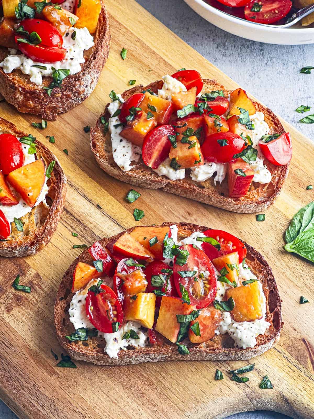 Three slices of bread with peaches, tomatoes, and burrata cheese on them.