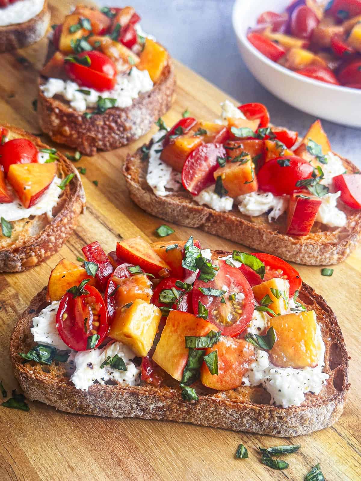 Fresh peaches, tomatoes, and burrata cheese on toasted bread slices.