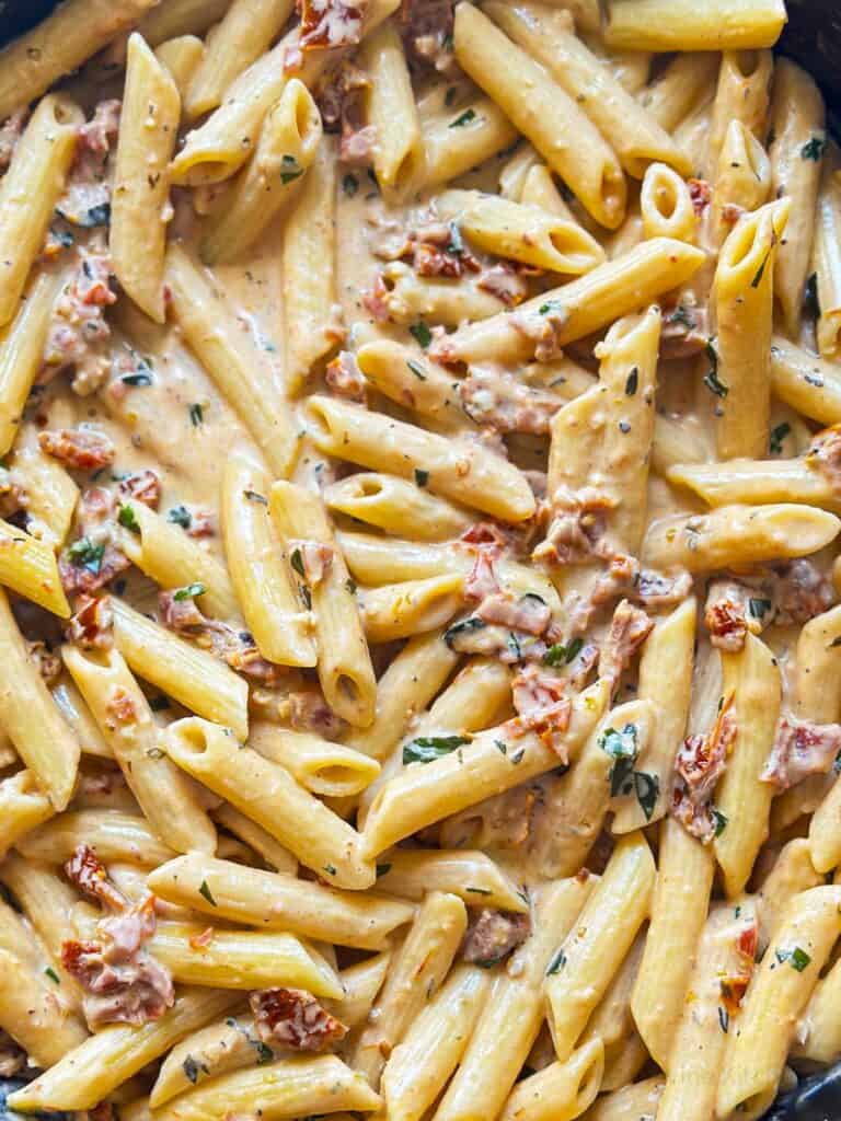 Close up of penne pasta in a creamy sauce with sun-dried tomatoes and basil.