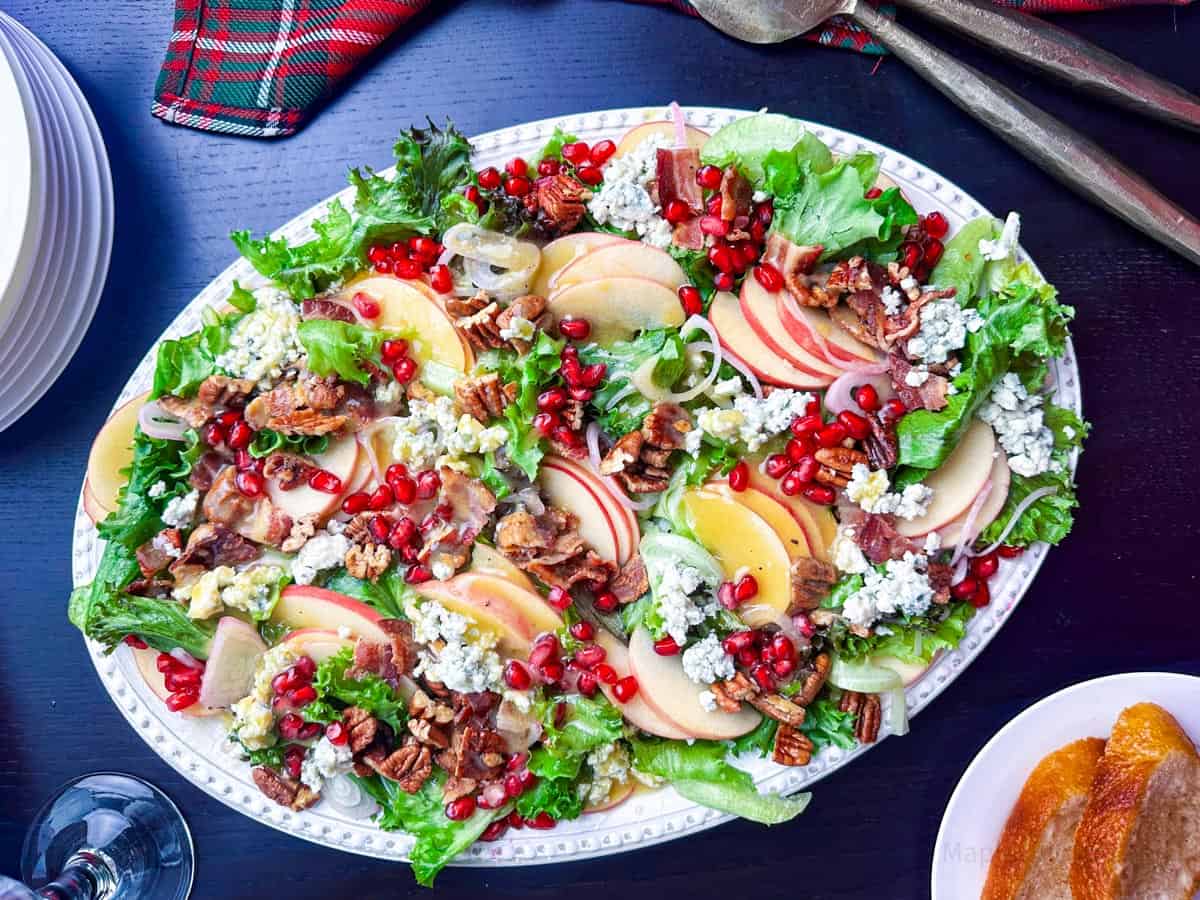 Fresh mixed greens salad with apples, pecans, blue cheese, and pomegranate seeds on a white platter.