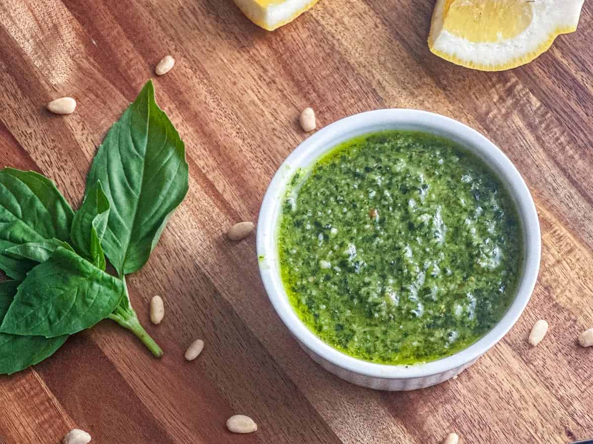 Basil pesto in a ramekin on a wooden board.