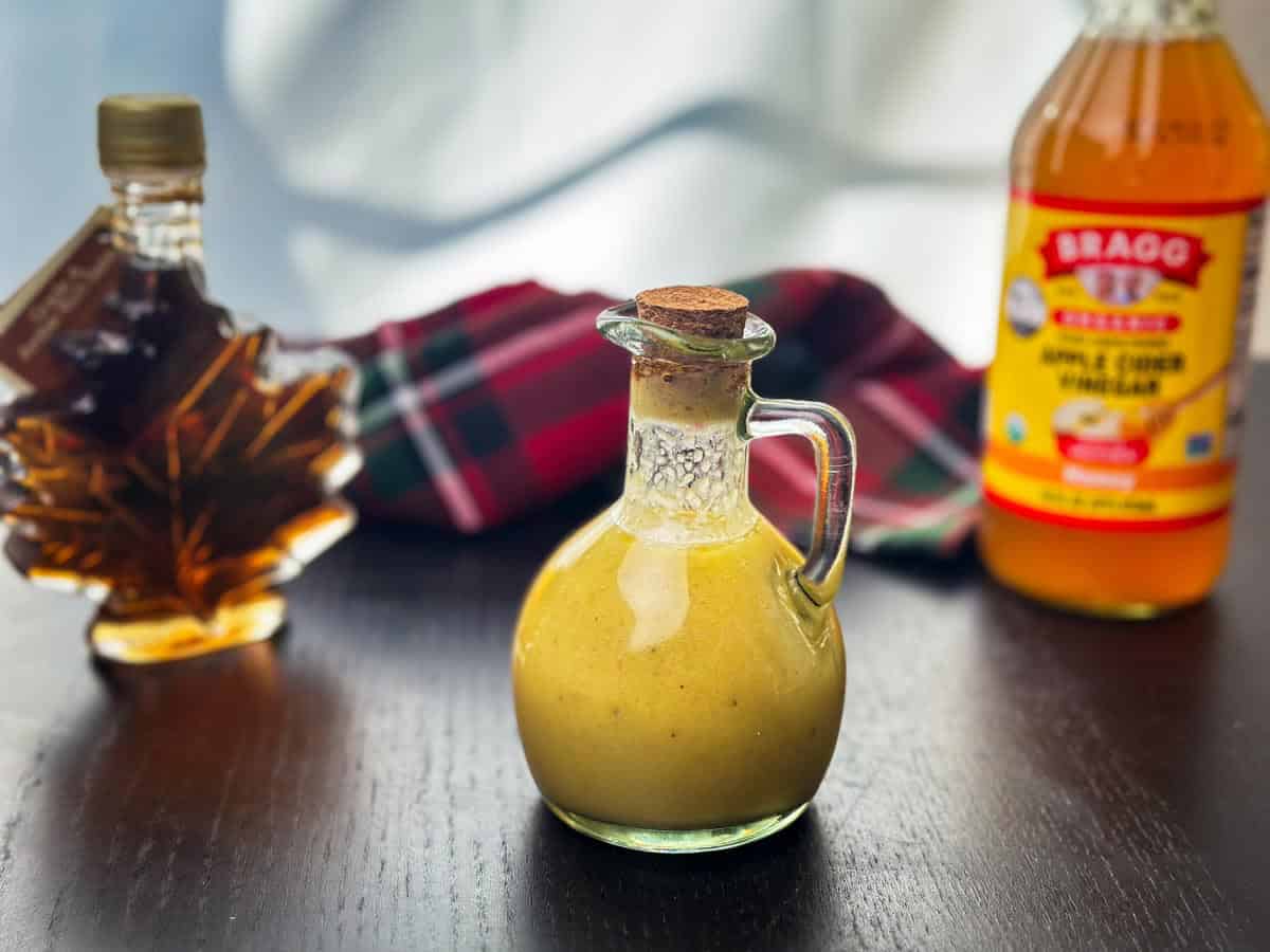 Creamy homemade apple cider vinaigrette in a glass bottle on a dark wooden table.