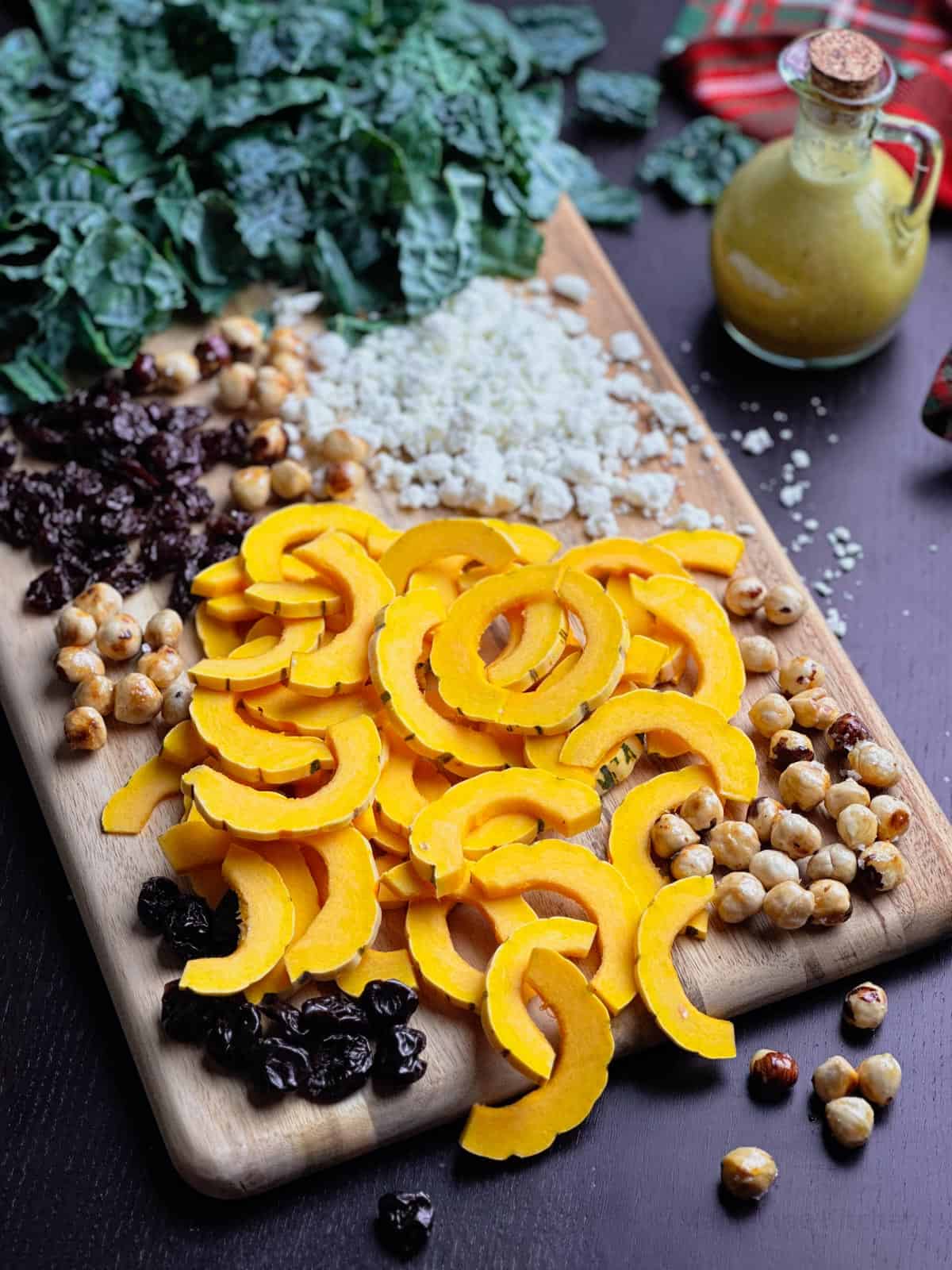 Delicata squash slices, dried cherries, hazelnuts, goat cheese, kale, and apple cider vinaigrette on a wooden cutting board.