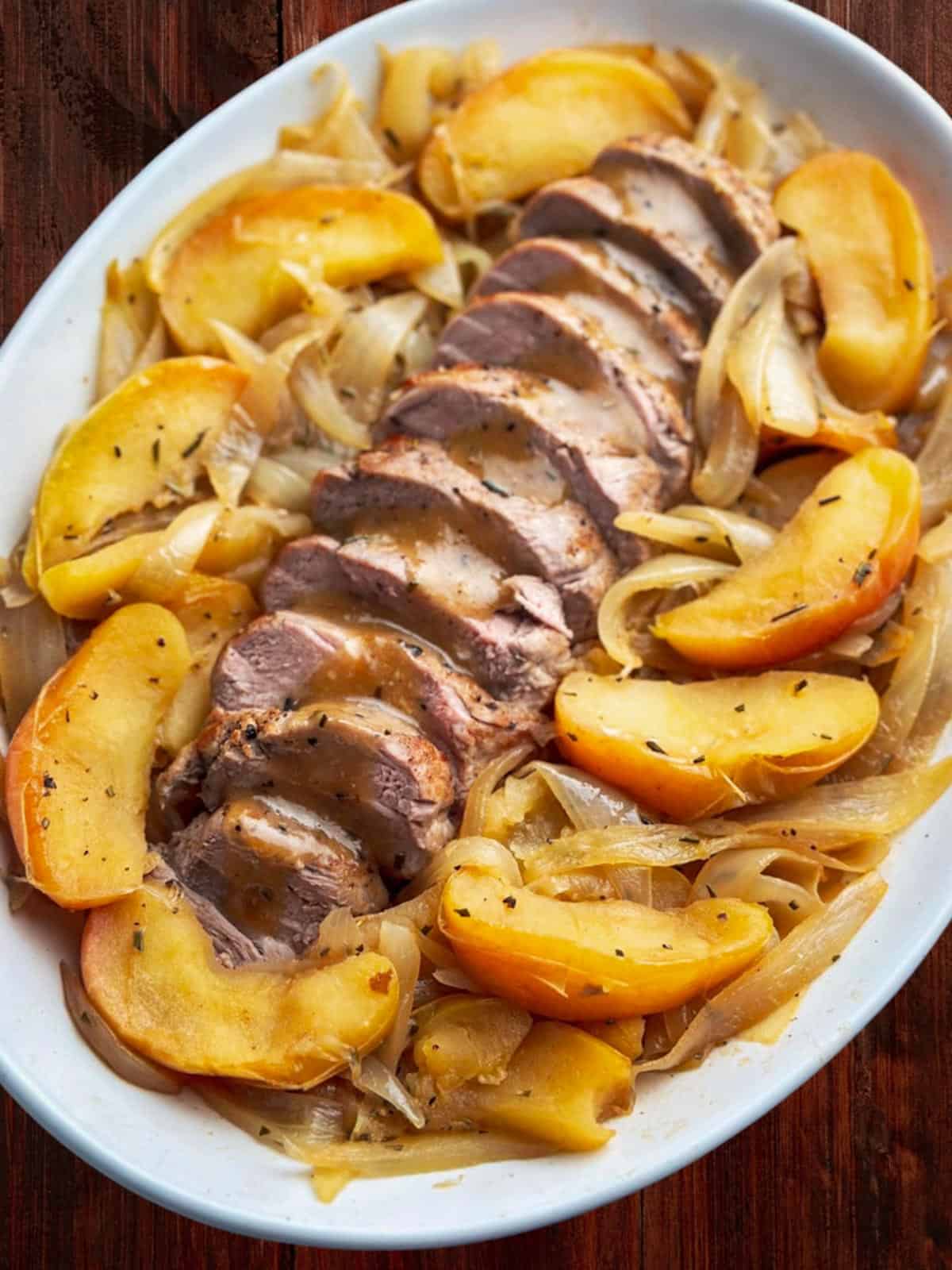 Sliced pork tenderloin with roasted apples and caramelized onions on a white serving dish.