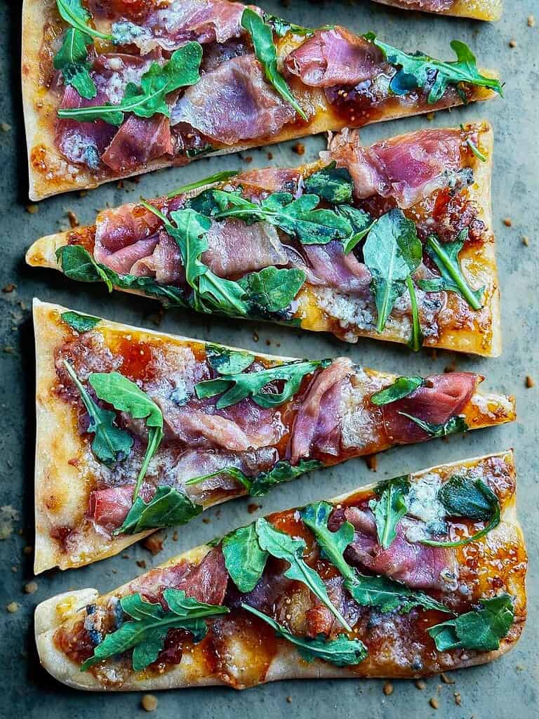 Fresh gourmet pizza slices with arugula, prosciutto, and blue cheese.