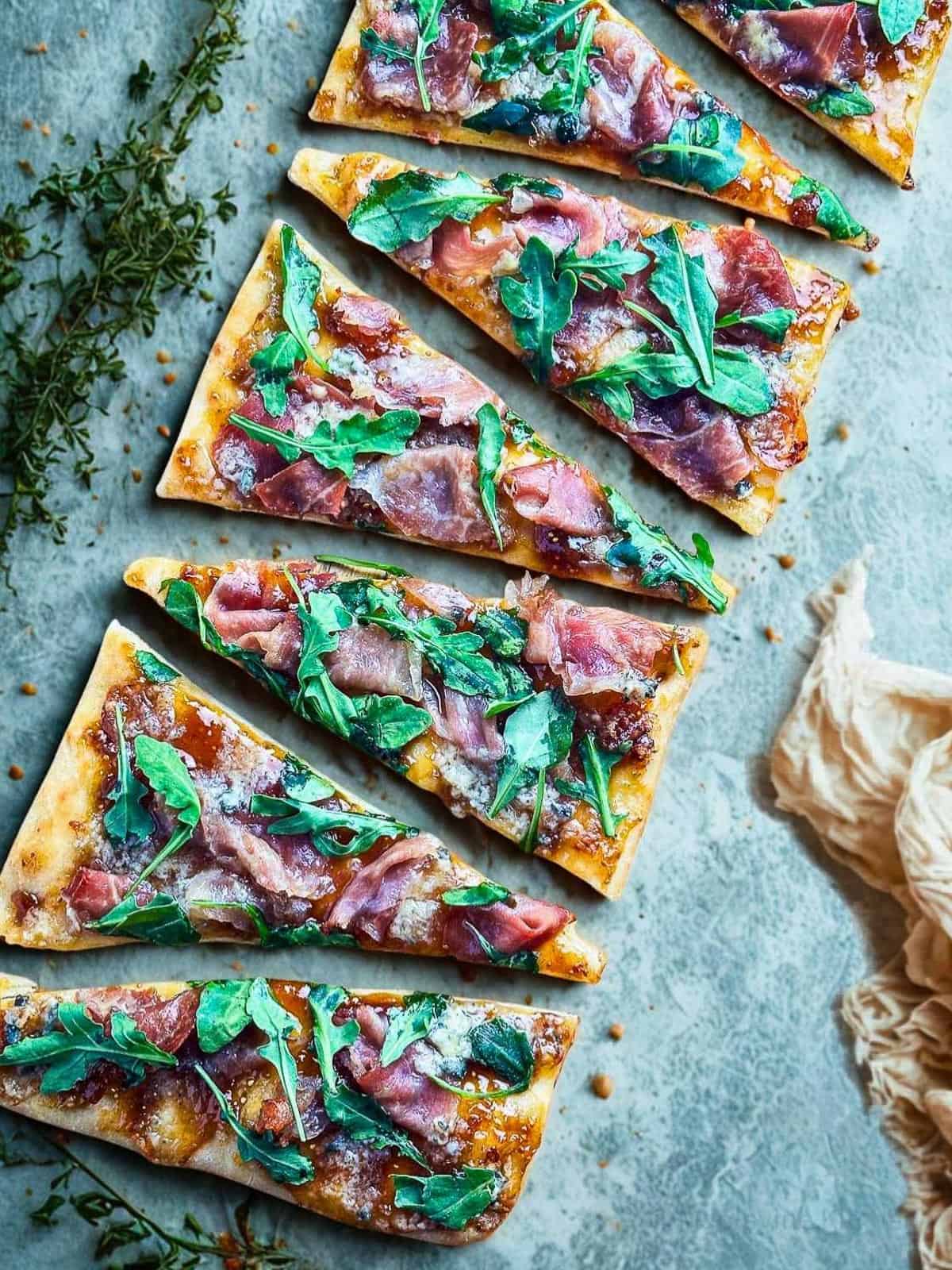 Gourmet flatbread pizza topped with prosciutto, arugula, and blue cheese, served on a rustic surface.