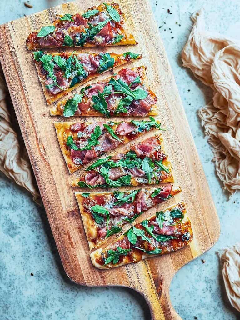Delicious flatbread topped prosciutto, fig jam, and blue cheese on a wooden serving board.