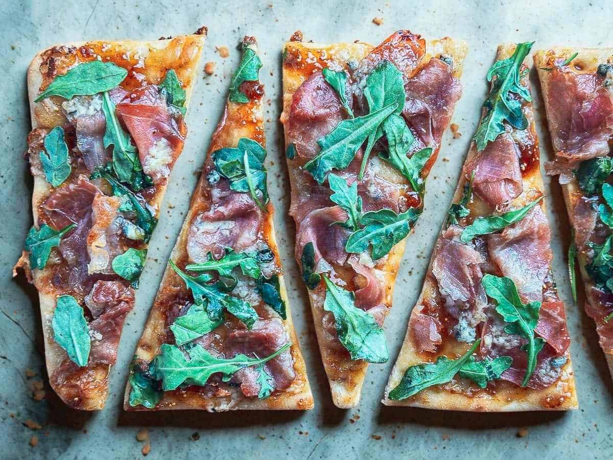 Prosciutto, fig jam, blue cheese, and fresh arugula on crispy flatbread, perfect for a quick gourmet snack or app.