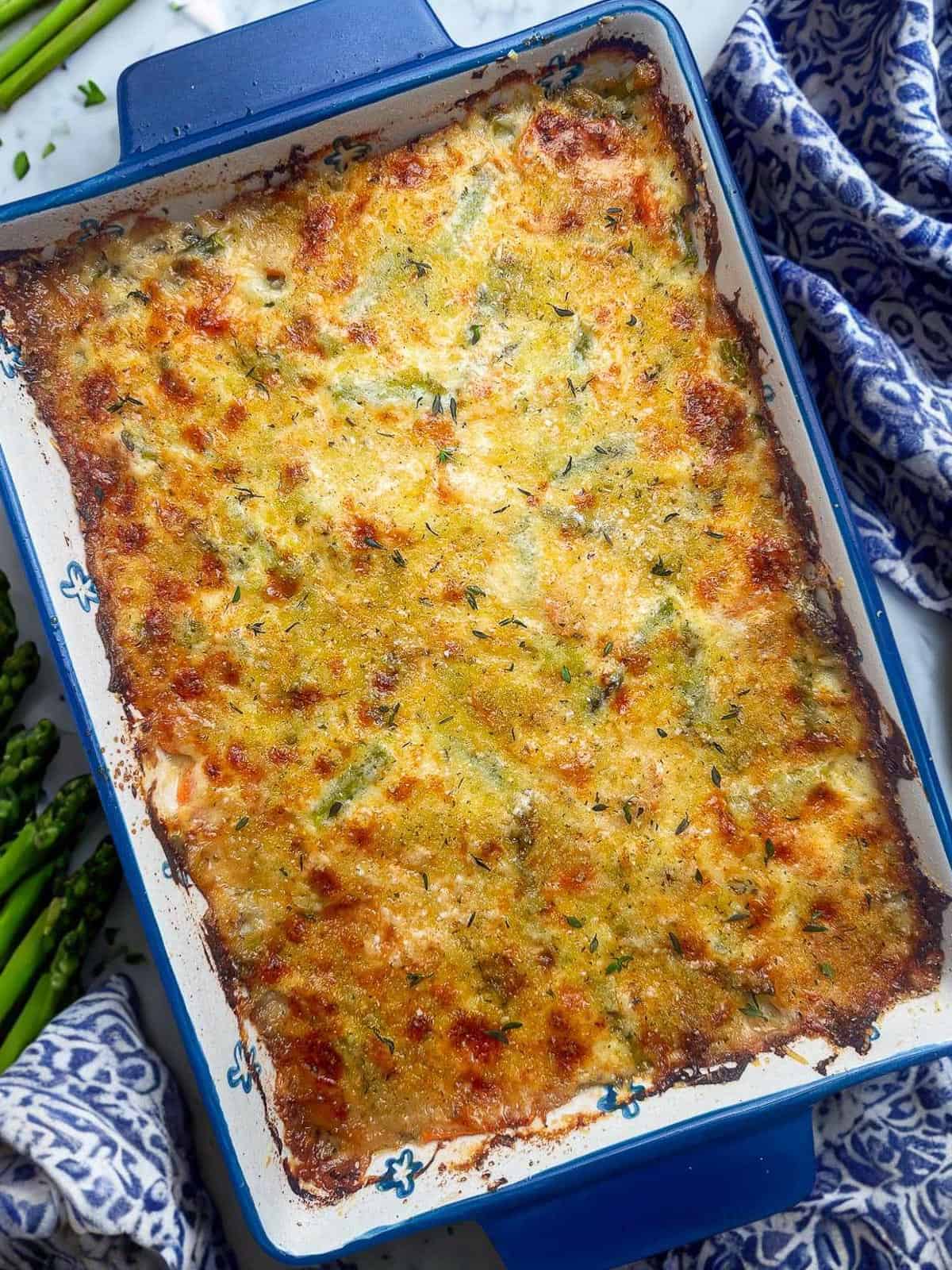 Spring vegetable au gratin casserole in a blue dish with fresh asparagus.