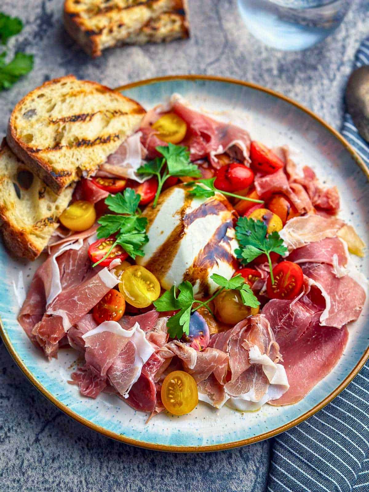 Burrata, prosciutto, cherry tomatoes, and fresh herbs on a stylish plate.