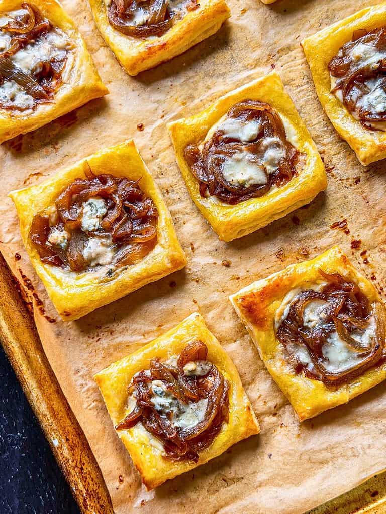 Caramelized onion puff pastry tarts with Gorgonzola on a baking sheet.