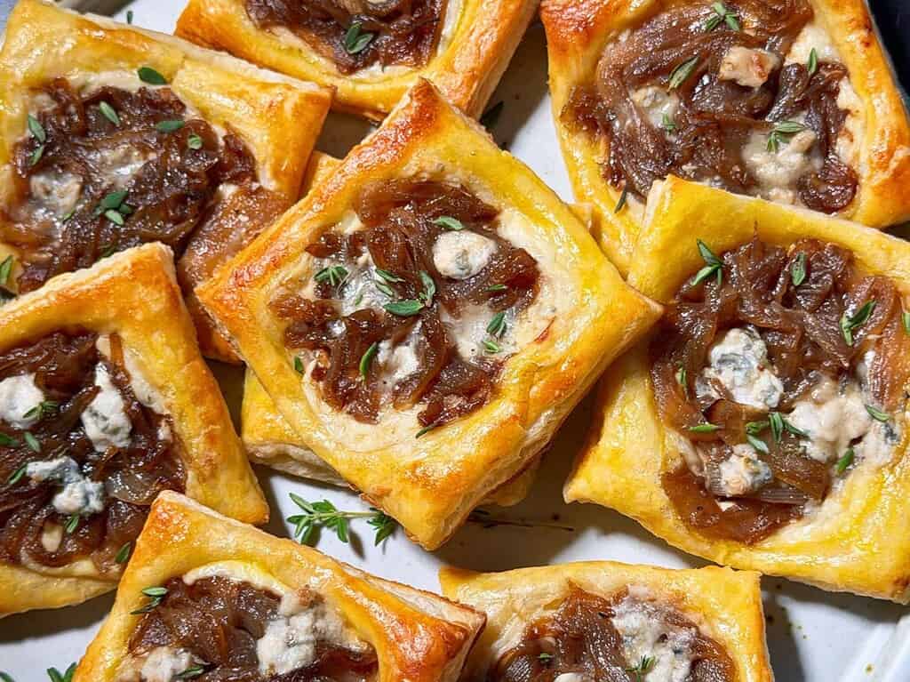 Caramelized onion puff pastry tarts with Gorgonzola and thyme layered on a plate.